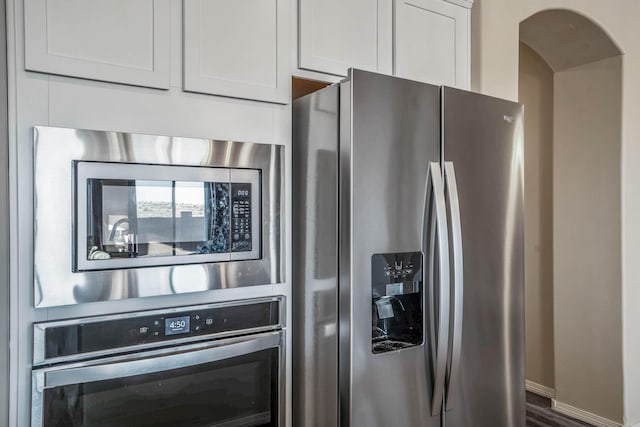 kitchen featuring arched walkways, white cabinets, and stainless steel appliances