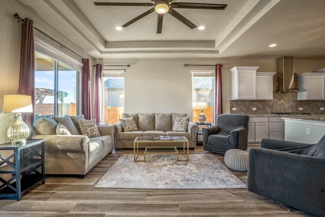 living area featuring a tray ceiling, plenty of natural light, wood finished floors, and ceiling fan