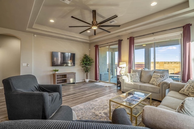 living area featuring wood finished floors, recessed lighting, arched walkways, a raised ceiling, and ceiling fan