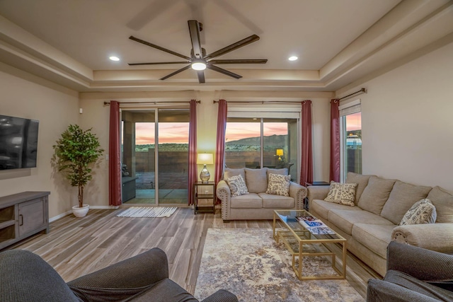 living room with a tray ceiling, baseboards, wood finished floors, and a ceiling fan