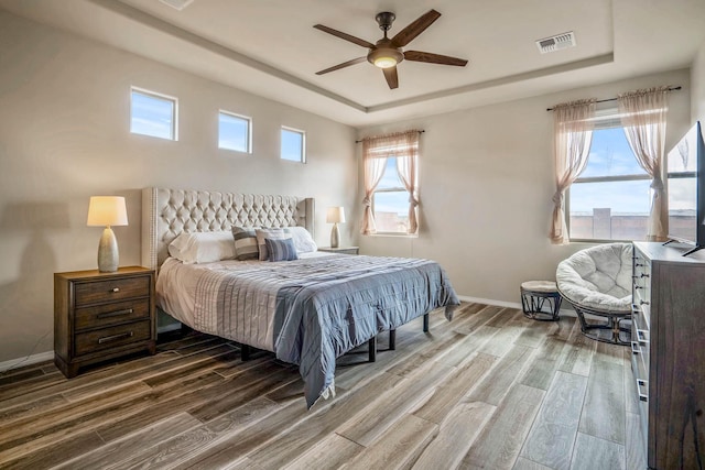 bedroom with a tray ceiling, wood finished floors, and visible vents