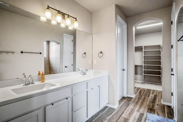 bathroom with double vanity, a spacious closet, wood finished floors, and a sink