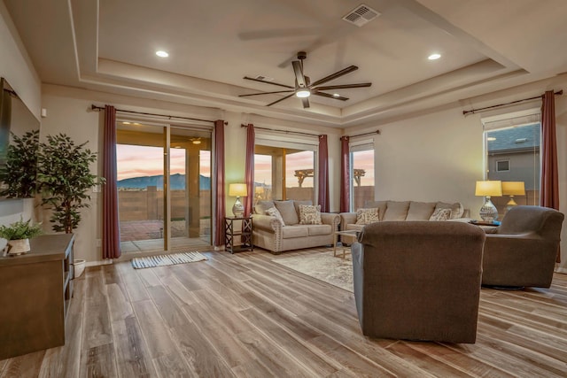 living area featuring a wealth of natural light, visible vents, light wood-style flooring, and a tray ceiling