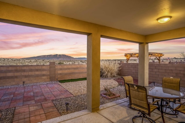 patio terrace at dusk with outdoor dining space, a fenced backyard, and a mountain view