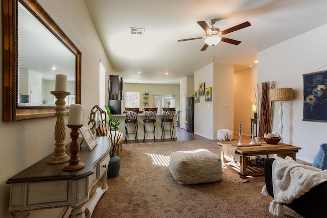 living area with carpet floors, visible vents, ceiling fan, and baseboards