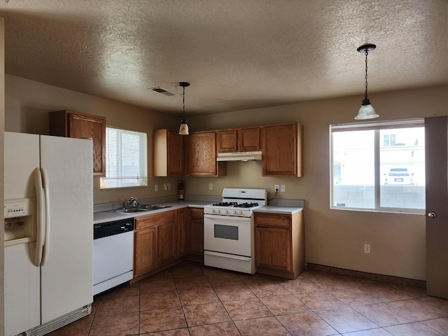 kitchen featuring visible vents, under cabinet range hood, light countertops, brown cabinetry, and white appliances