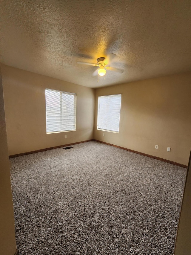 empty room featuring visible vents, a textured ceiling, carpet flooring, baseboards, and ceiling fan