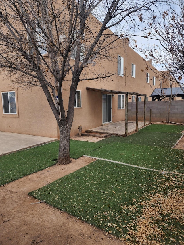 rear view of property featuring stucco siding, fence, a lawn, and a patio area