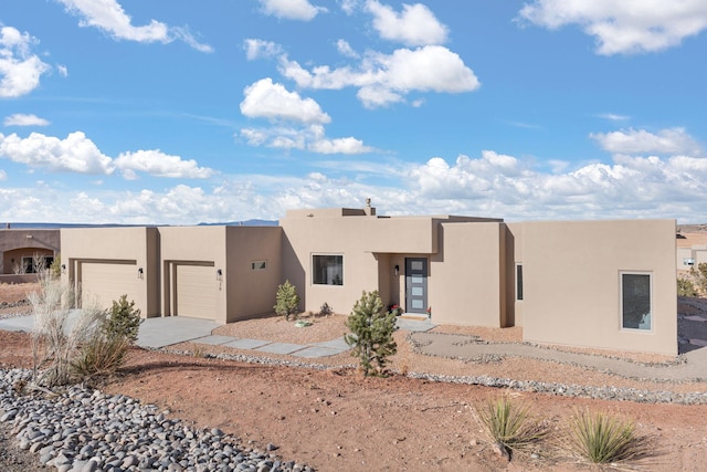 pueblo-style house with concrete driveway, an attached garage, and stucco siding