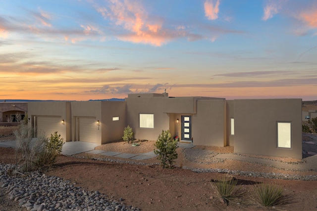 pueblo-style home with an attached garage, driveway, and stucco siding