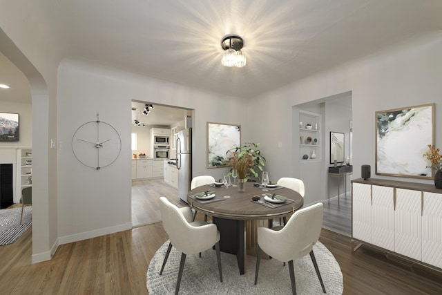 dining space with arched walkways, a fireplace, light wood-style flooring, and baseboards