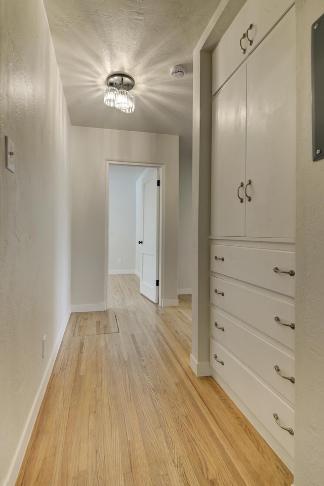 hallway featuring light wood-type flooring, a textured ceiling, and baseboards