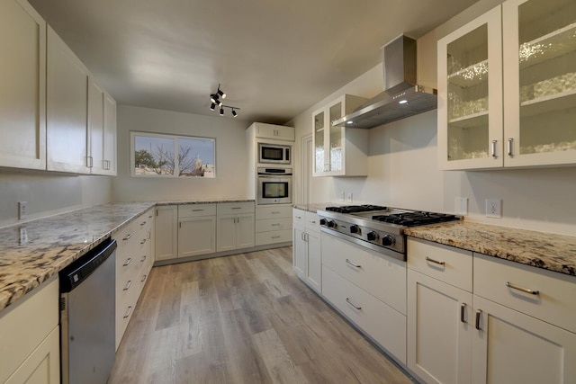 kitchen with light stone counters, light wood finished floors, appliances with stainless steel finishes, white cabinetry, and wall chimney exhaust hood