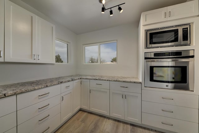 kitchen featuring light wood-type flooring, white cabinetry, appliances with stainless steel finishes, and light stone counters