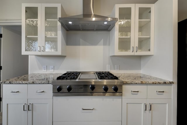 kitchen with light stone counters, white cabinetry, stainless steel gas stovetop, and wall chimney range hood