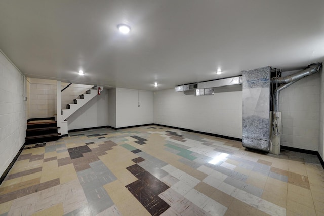 finished below grade area featuring stairs, tile patterned floors, concrete block wall, and heating unit