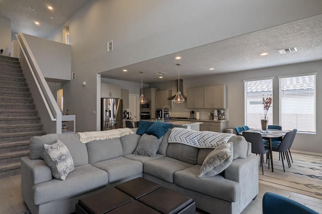 living area with light wood-style floors, visible vents, a textured ceiling, and stairs