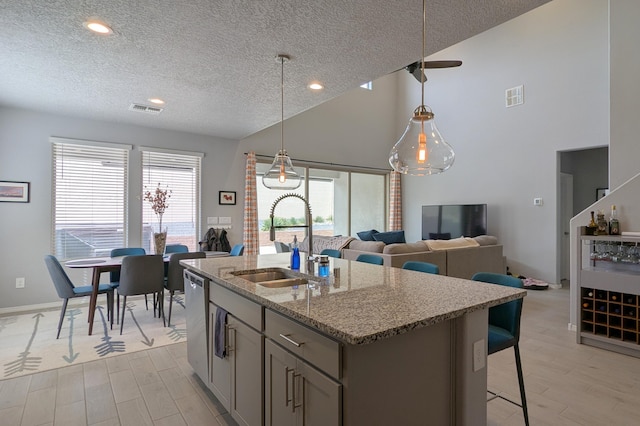 kitchen with a kitchen island with sink, light stone counters, a sink, and visible vents