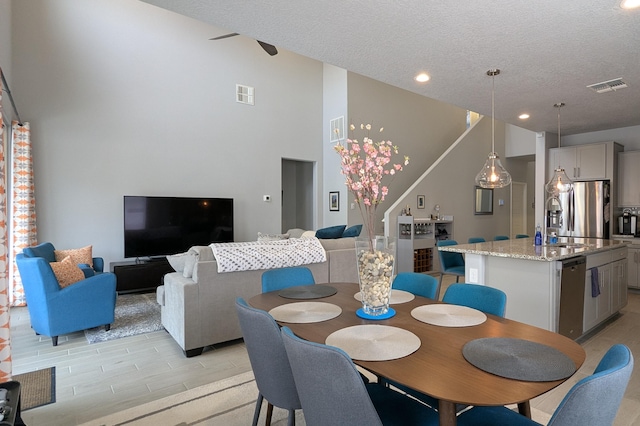 dining space featuring a towering ceiling, visible vents, a textured ceiling, and recessed lighting