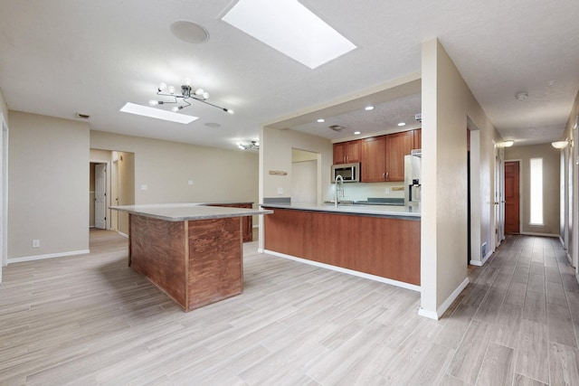 kitchen featuring a skylight, baseboards, brown cabinetry, stainless steel appliances, and light wood-style floors