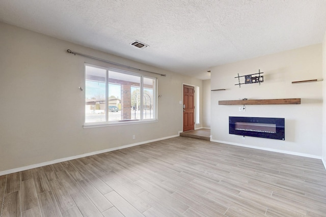 unfurnished living room with visible vents, a glass covered fireplace, a textured ceiling, light wood-type flooring, and baseboards