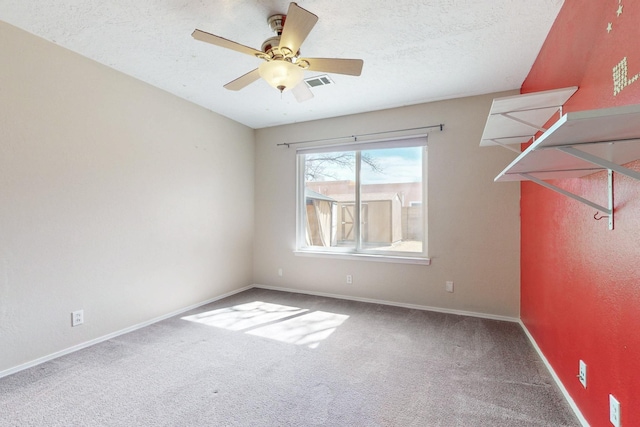 carpeted spare room featuring a ceiling fan, visible vents, baseboards, and a textured ceiling