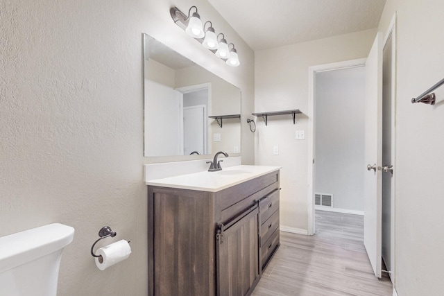 half bathroom with toilet, wood finished floors, vanity, visible vents, and baseboards