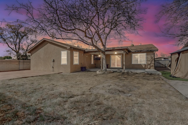 rear view of property featuring a patio area, fence, and stucco siding