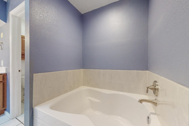 bathroom featuring a textured wall, toilet, vanity, a bath, and tile patterned floors