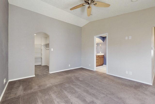 empty room with arched walkways, ceiling fan, lofted ceiling, light colored carpet, and baseboards