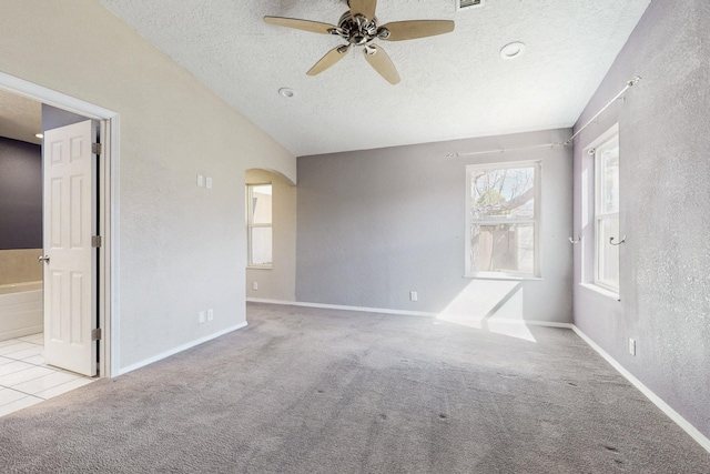 carpeted spare room featuring baseboards, arched walkways, a ceiling fan, lofted ceiling, and a textured ceiling