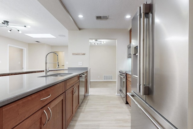 kitchen with a skylight, visible vents, appliances with stainless steel finishes, brown cabinets, and a sink