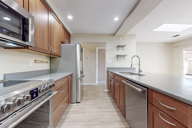 kitchen with light wood-style flooring, stainless steel appliances, a sink, visible vents, and brown cabinets