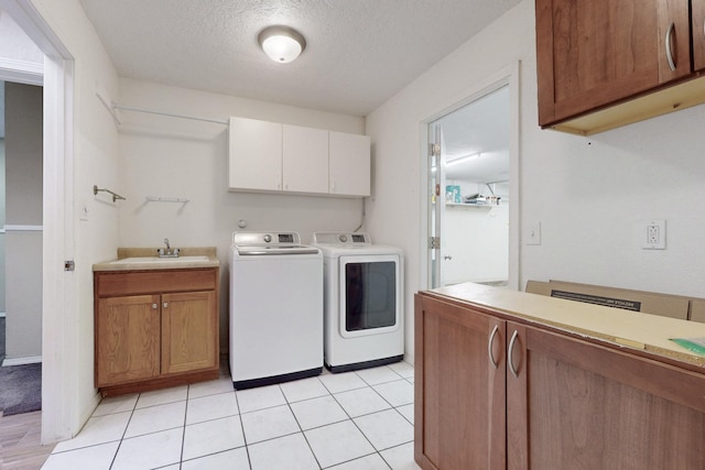 laundry area featuring light tile patterned floors, cabinet space, a sink, a textured ceiling, and independent washer and dryer