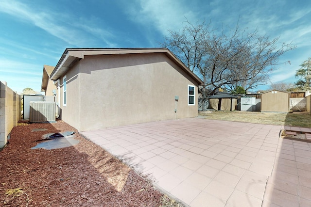 rear view of property featuring an outbuilding, a storage shed, central AC, stucco siding, and a patio area