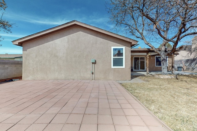 rear view of house with a lawn, a patio area, fence, and stucco siding