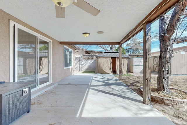 view of patio / terrace with ceiling fan, a storage unit, a fenced backyard, and an outbuilding