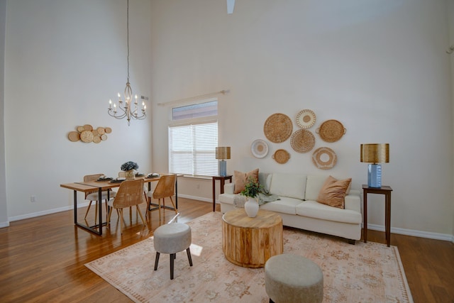 living area with a chandelier, a high ceiling, wood finished floors, and baseboards