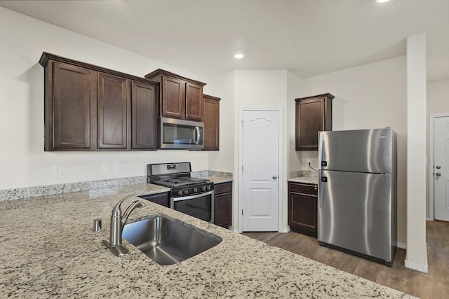 kitchen featuring dark brown cabinetry, light stone counters, stainless steel appliances, and a sink