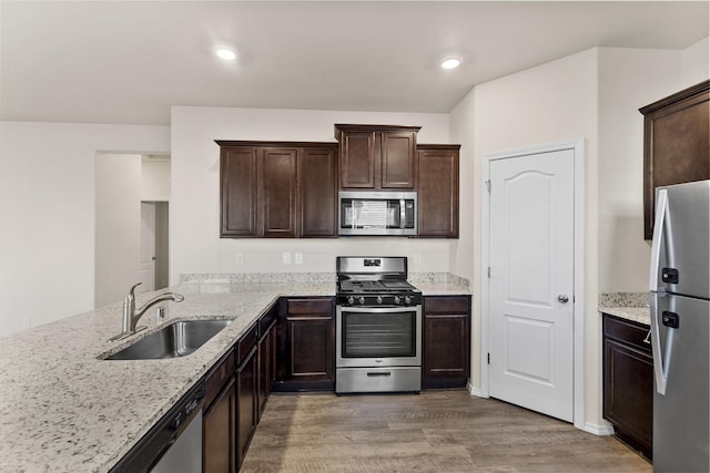 kitchen with appliances with stainless steel finishes, a sink, light stone counters, and dark brown cabinets