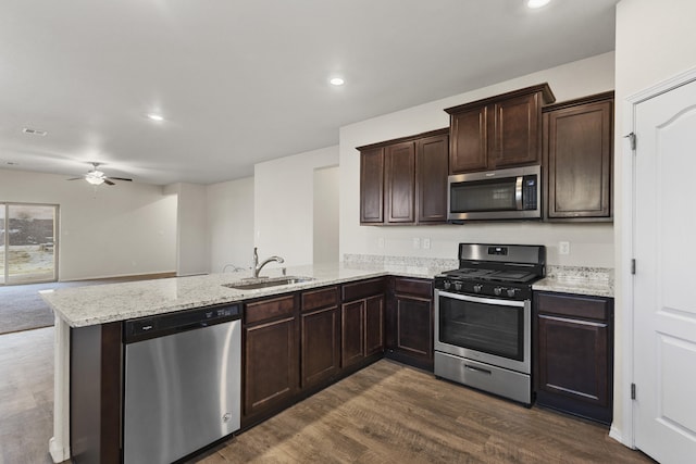 kitchen featuring appliances with stainless steel finishes, dark wood-style flooring, a peninsula, dark brown cabinets, and a sink