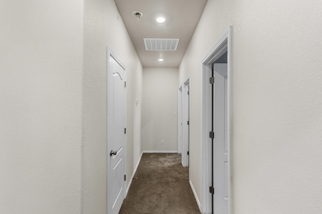 corridor with baseboards, visible vents, and dark carpet