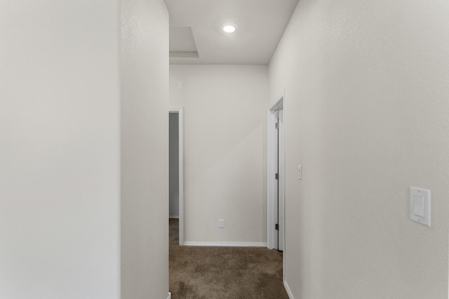 hallway featuring dark colored carpet and baseboards