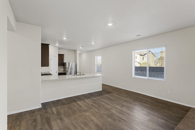 kitchen with dark wood-type flooring, freestanding refrigerator, a sink, a peninsula, and baseboards