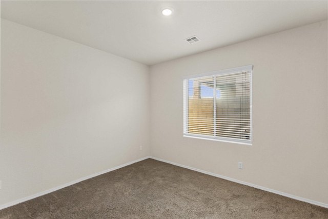 spare room featuring dark colored carpet, visible vents, and baseboards