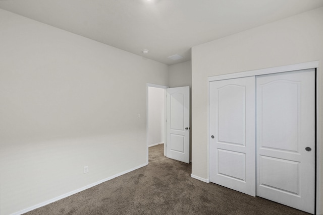 unfurnished bedroom with baseboards, dark carpet, and a closet