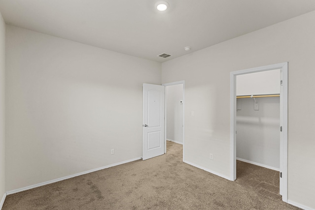 unfurnished bedroom with a closet, carpet, a walk in closet, and baseboards