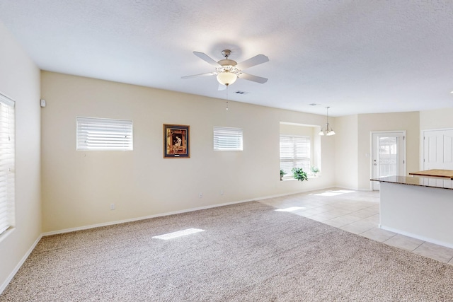 spare room featuring a textured ceiling, light tile patterned flooring, light colored carpet, a ceiling fan, and visible vents