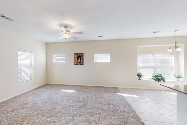 spare room with ceiling fan with notable chandelier, visible vents, baseboards, and light tile patterned flooring