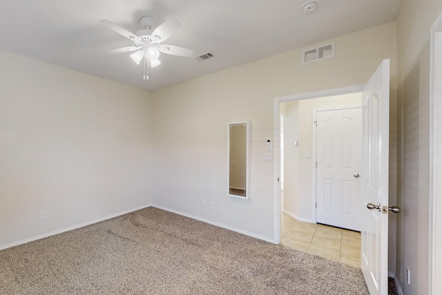 empty room featuring light carpet, light tile patterned flooring, visible vents, and a ceiling fan